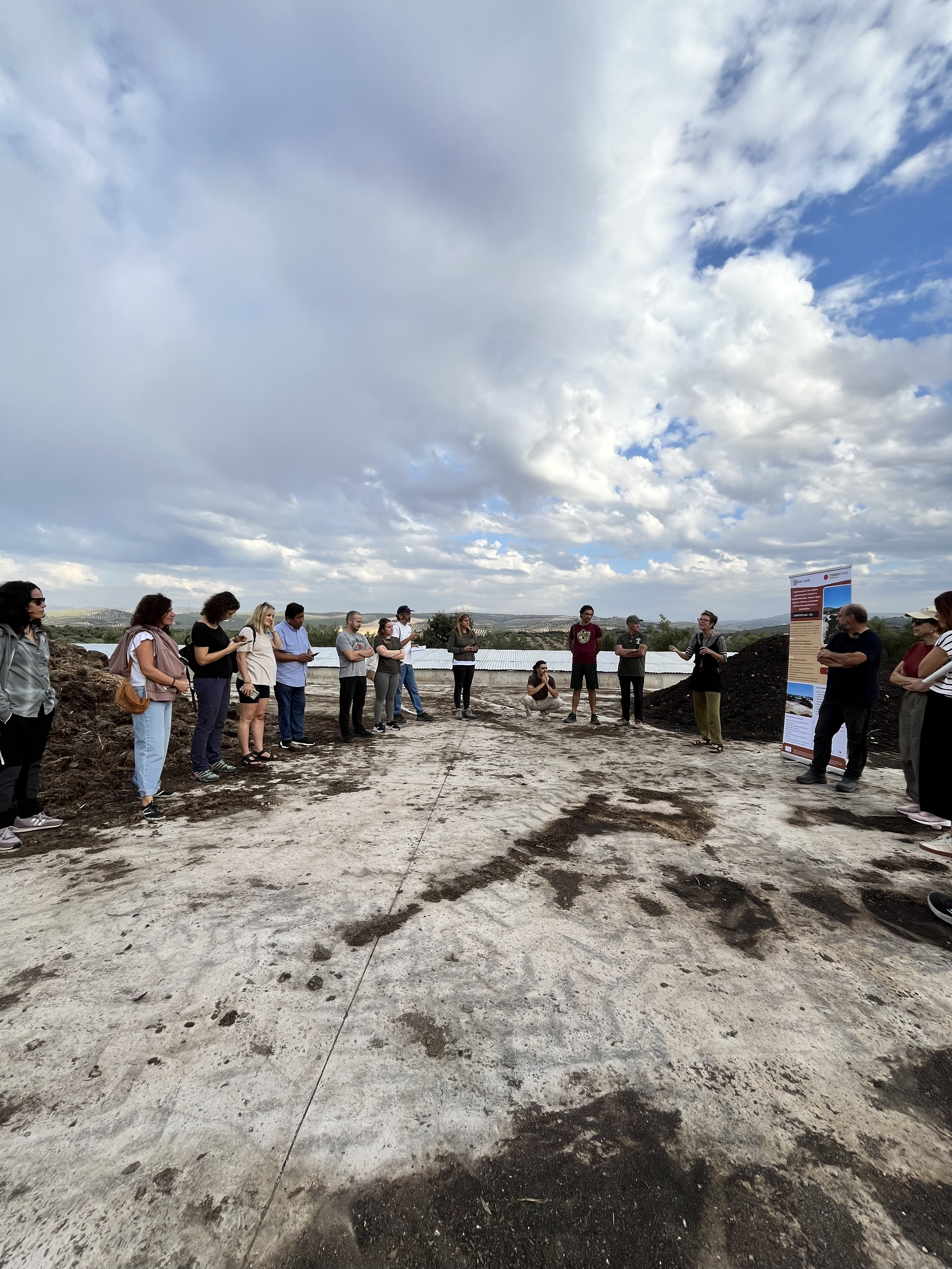 Participantes de pie junto a las pilas de compost y el panel del proyecto